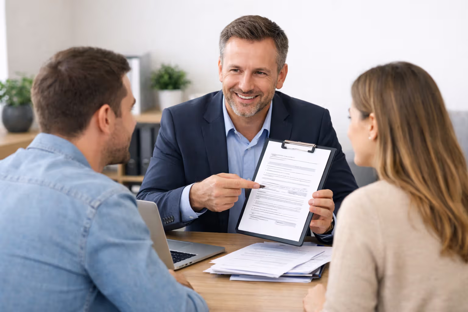 An independent insurance agent showing documents to a couple sitting across the desk in a modern office