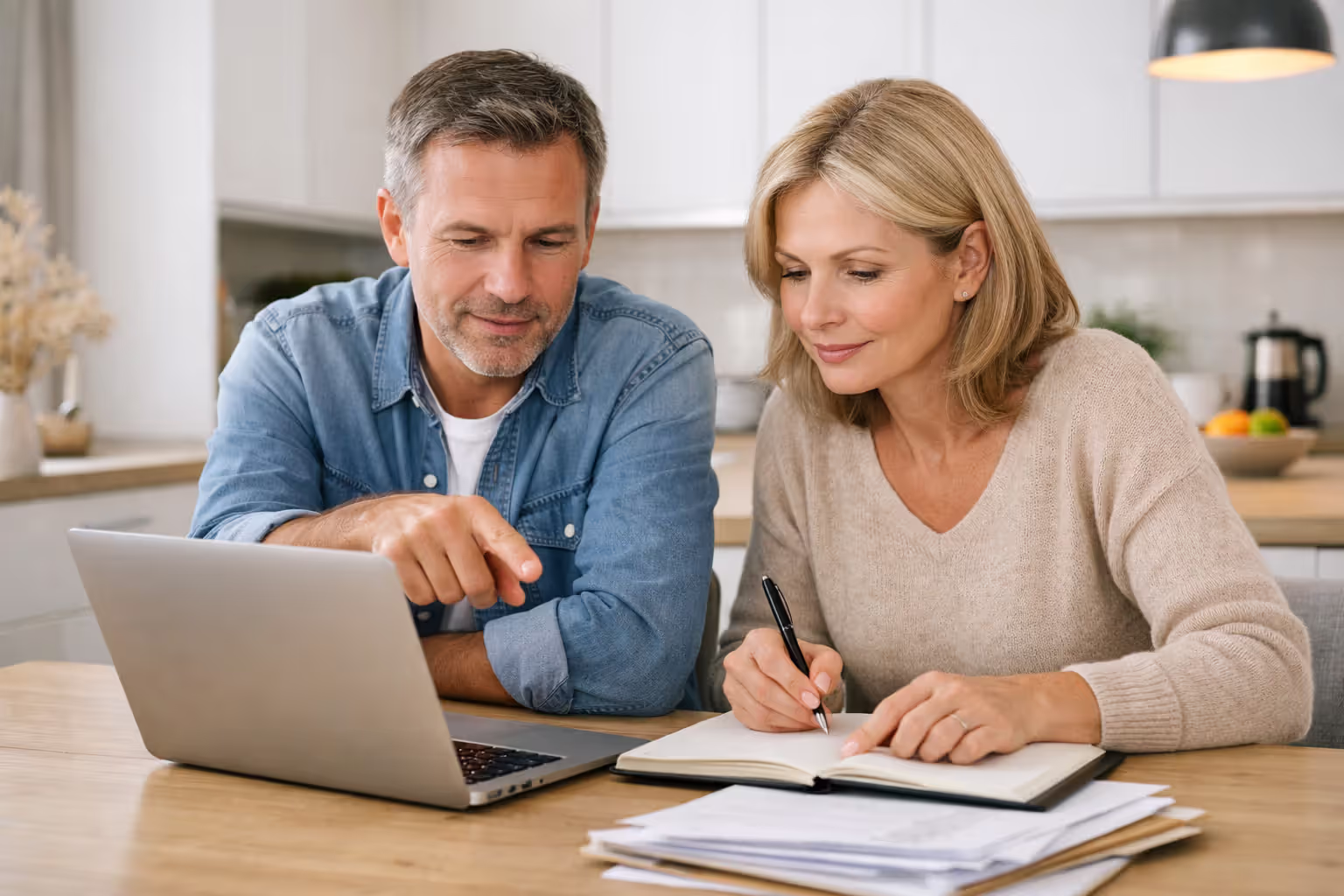 Couple reviewing their homeowners insurance policy documents together at a kitchen table with a laptop