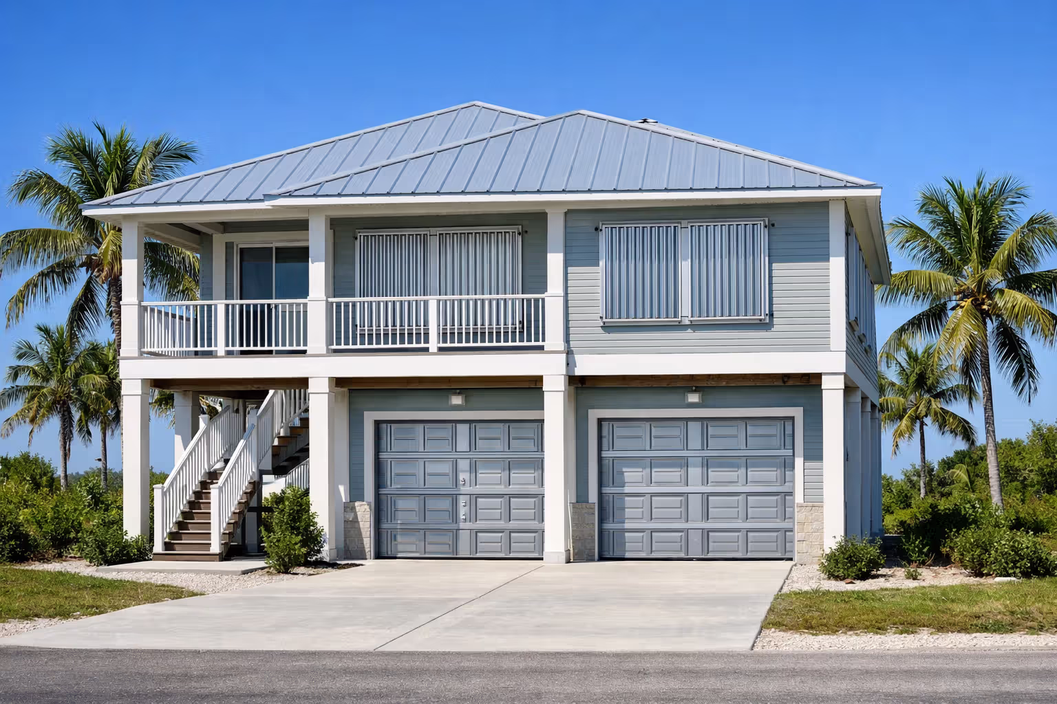 Elevated coastal home on stilts with hurricane shutters on windows, reinforced roof, and impact-resistant garage door with palm trees in background